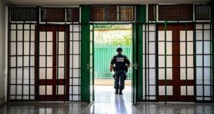 Agente de segurança de costas atravessando portão gradeado em corredor de prédio público
