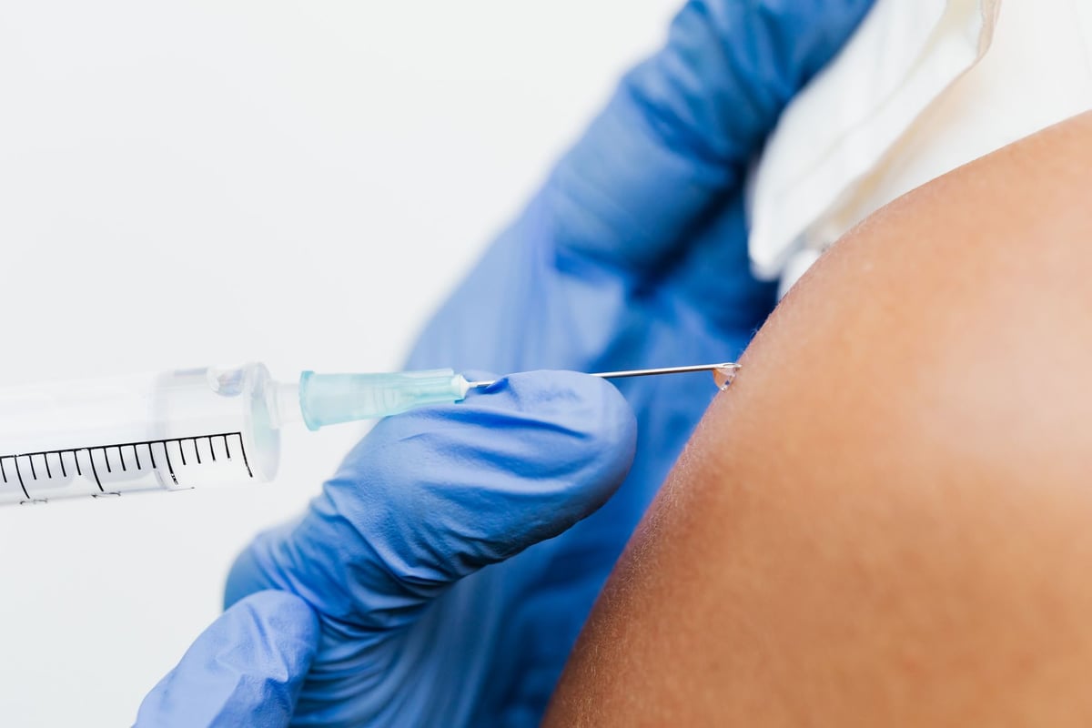Profissional de saúde aplica vacina no braço de paciente em posto de saúde