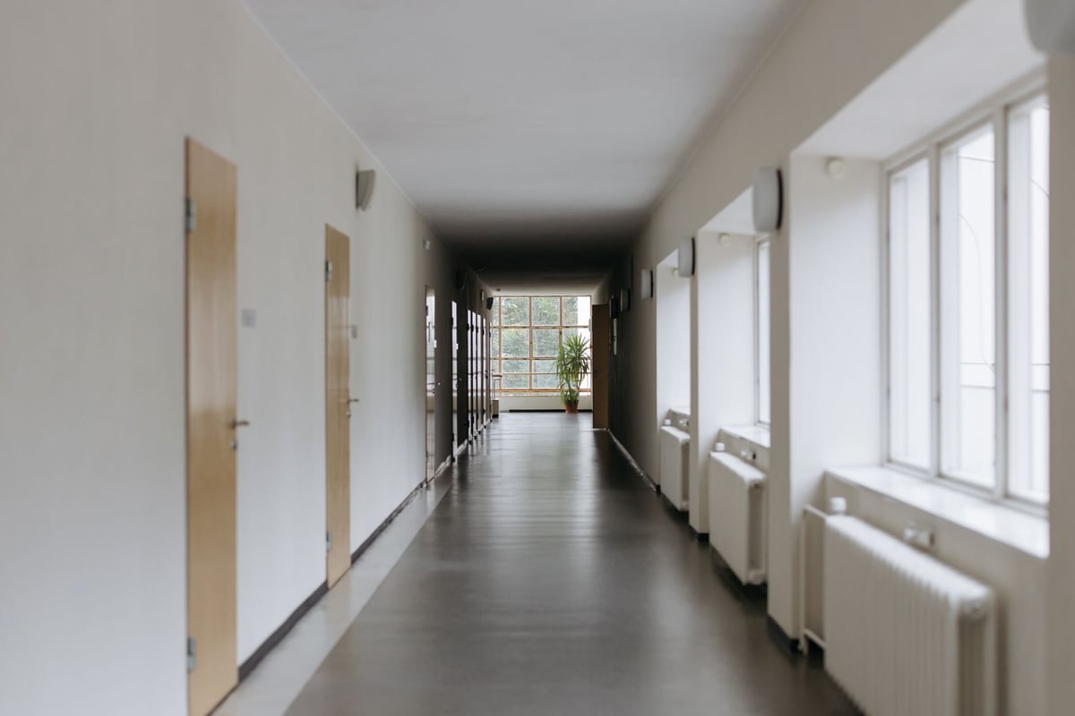Corredor de escola com mesas e cadeiras vazias, iluminado por luz natural