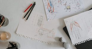 Mesa de trabalho com pranchetas, paleta de cores e materiais de design gráfico