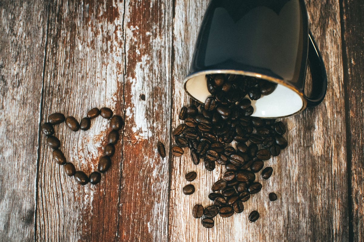 Grãos de café torrados e uma xícara de café sobre uma mesa de madeira