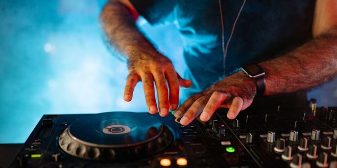 DJ manuseia mesa de som e toca-discos em cabine durante festa noturna