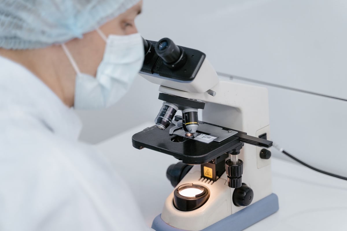 Profissional de saúde com máscara e luvas analisando amostra em laboratório