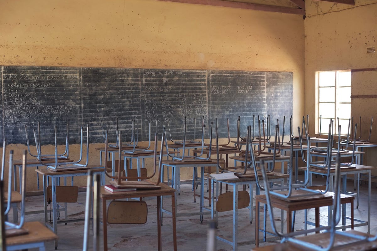 Mãos de criança segurando lápis de cor sobre mesa de sala de aula