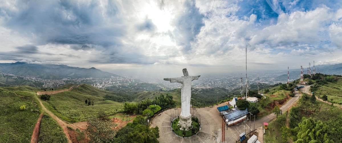 Estátua de braços abertos erguida no alto de um morro ao entardecer