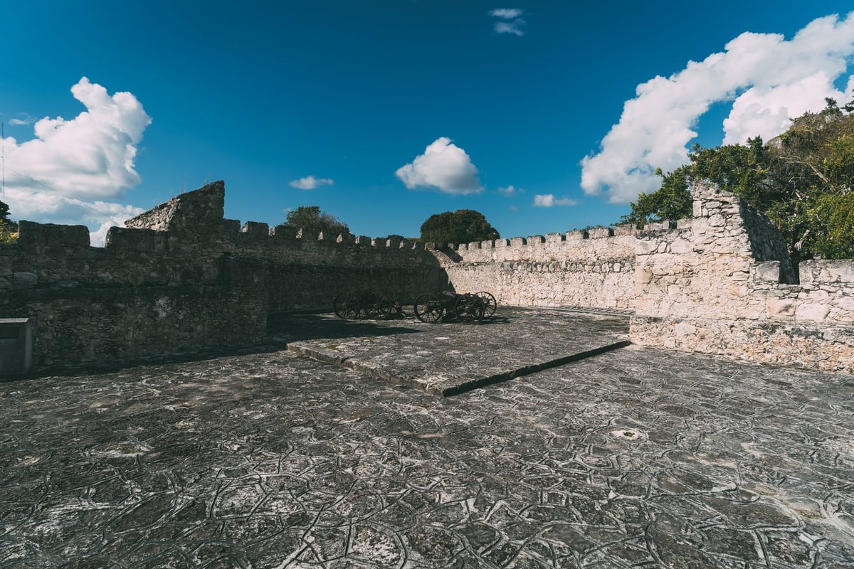 Muro de fortificação antiga de pedra sob céu claro, com poste de execução histórica ao centro