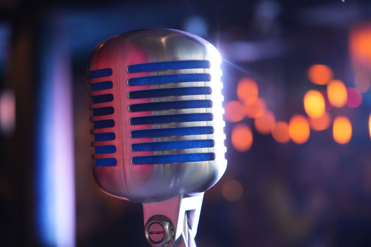 Microfone vintage de estúdio em primeiro plano com luzes de palco desfocadas ao fundo