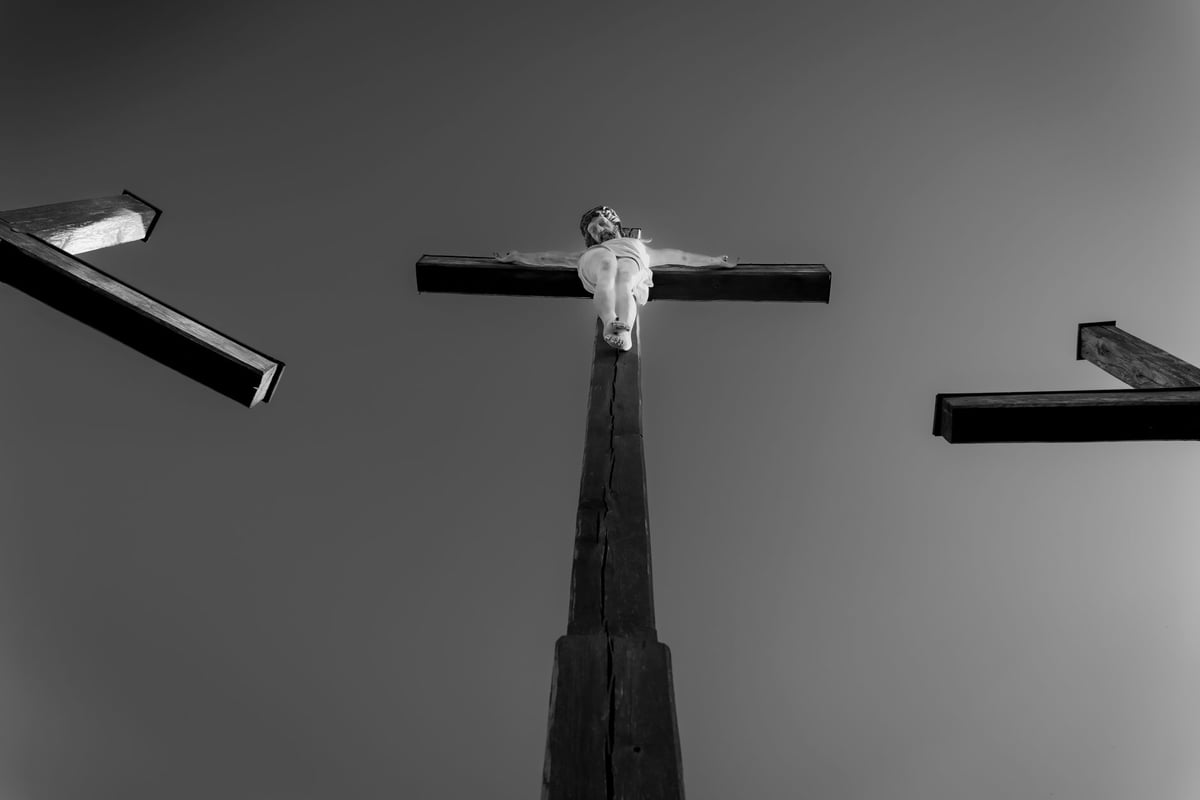 Imagem de crucifixo com figura de mulher de véu escuro apertada contra o peito de uma pessoa ajoelhada.
