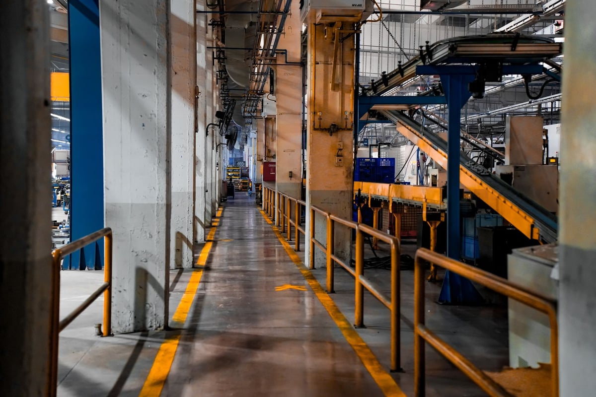 Linha de montagem de fábrica automotiva parada, com macacões pendurados e máquinas silenciosas.