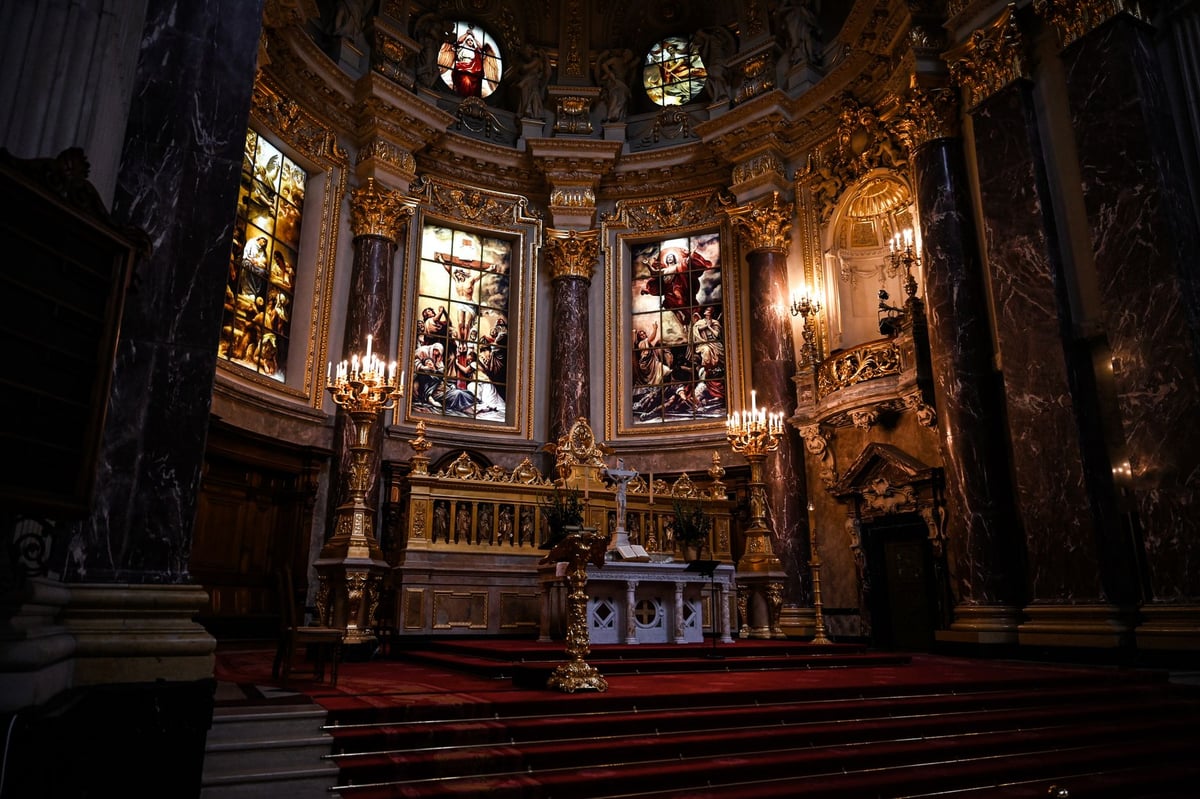 Vela acesa diante de imagem de santo em nicho de igreja, com flores ao redor