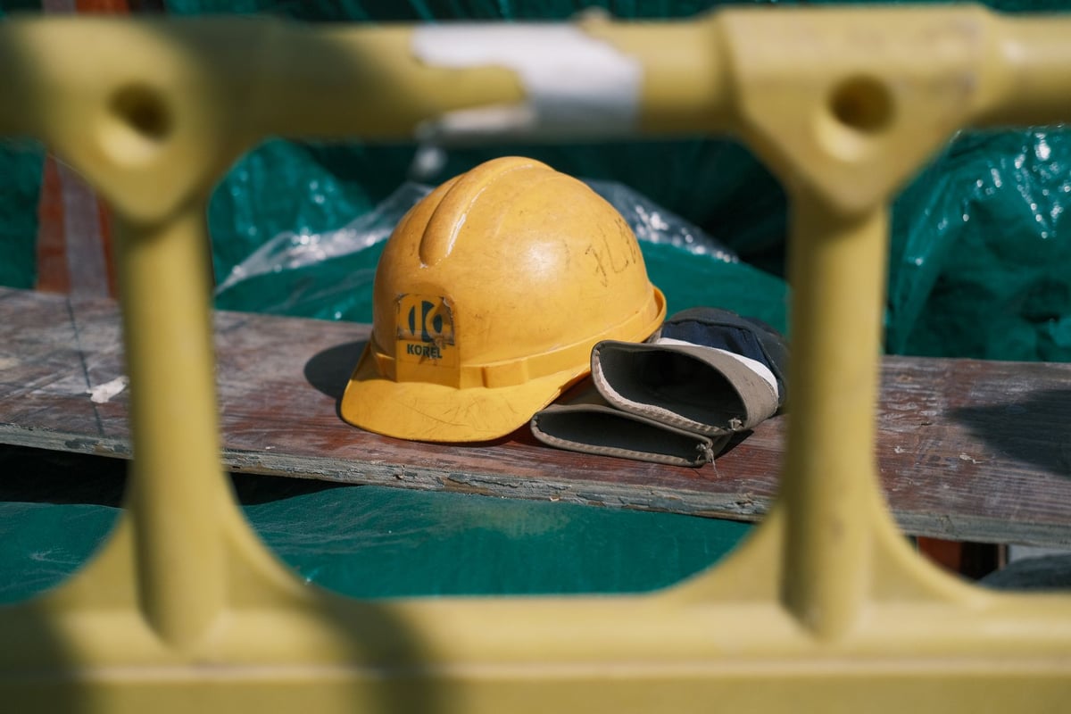Capacete de segurança e luvas de proteção apoiados sobre uma bancada de fábrica