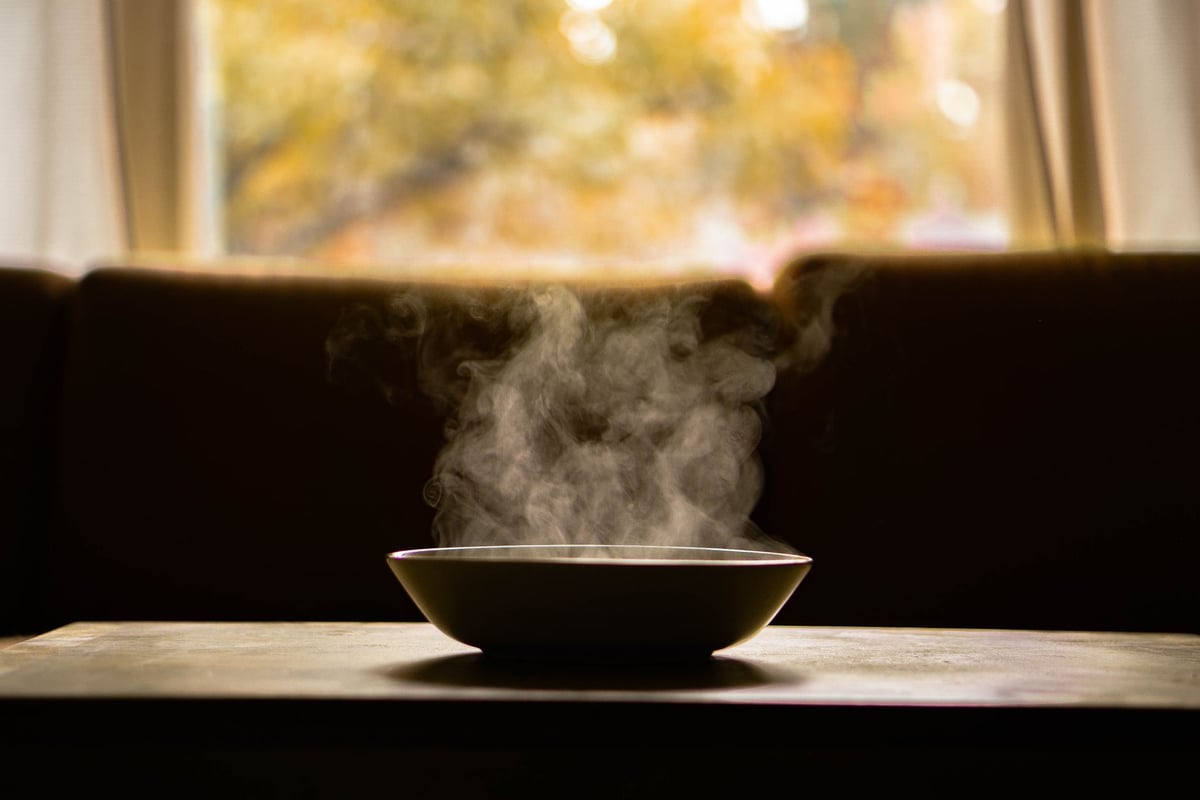 Mãos idosas segurando tigela de sopa em ambiente simples de acolhimento
