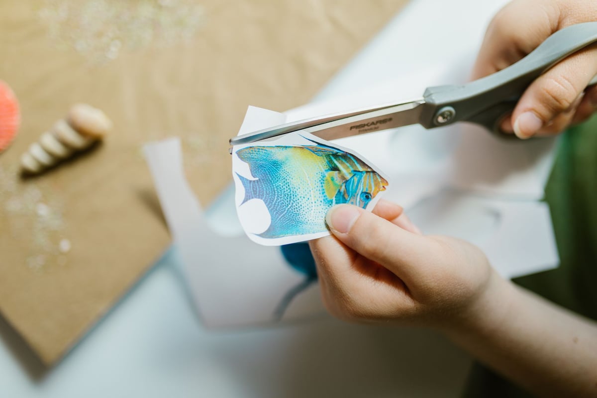 Mão segurando peixe de papel colorido recortado sobre fundo neutro