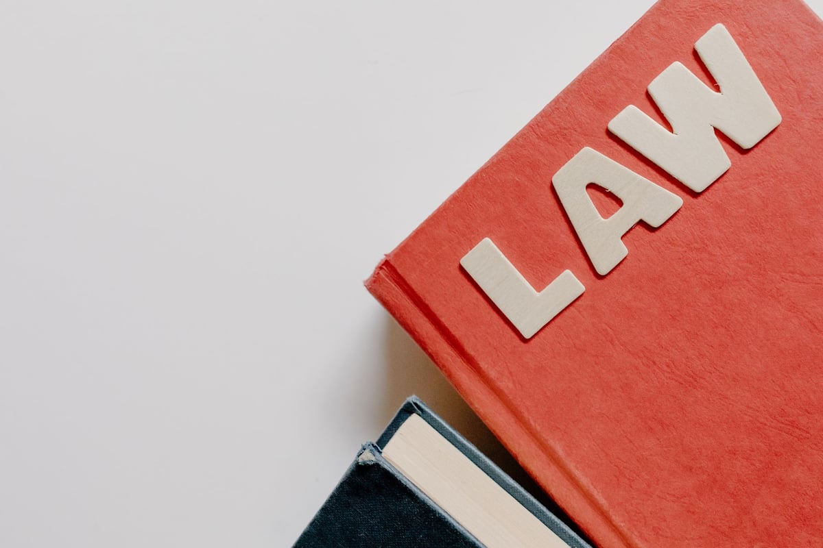 Livro de leis grosso aberto sobre mesa de escritório com óculos ao lado