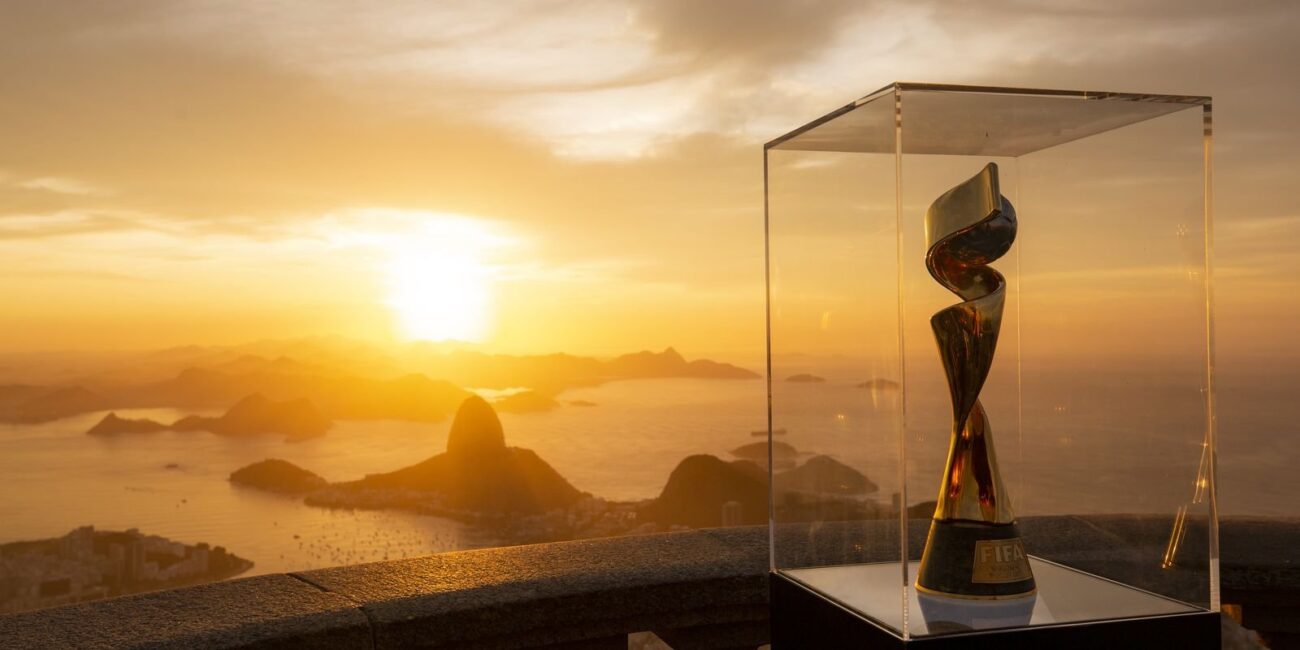 Troféu em vitrine de vidro com vista de pôr do sol sobre baía com montanhas e ilhas ao fundo